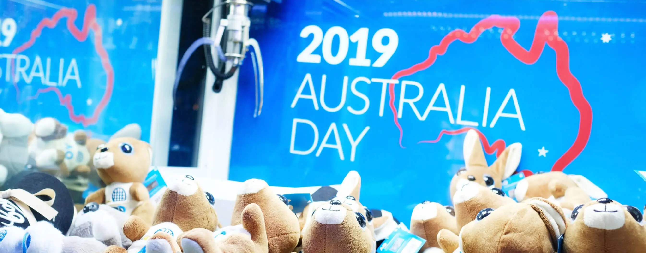 Inside of claw game with stuffed animals in foreground and design for Australia Day 2019 in background